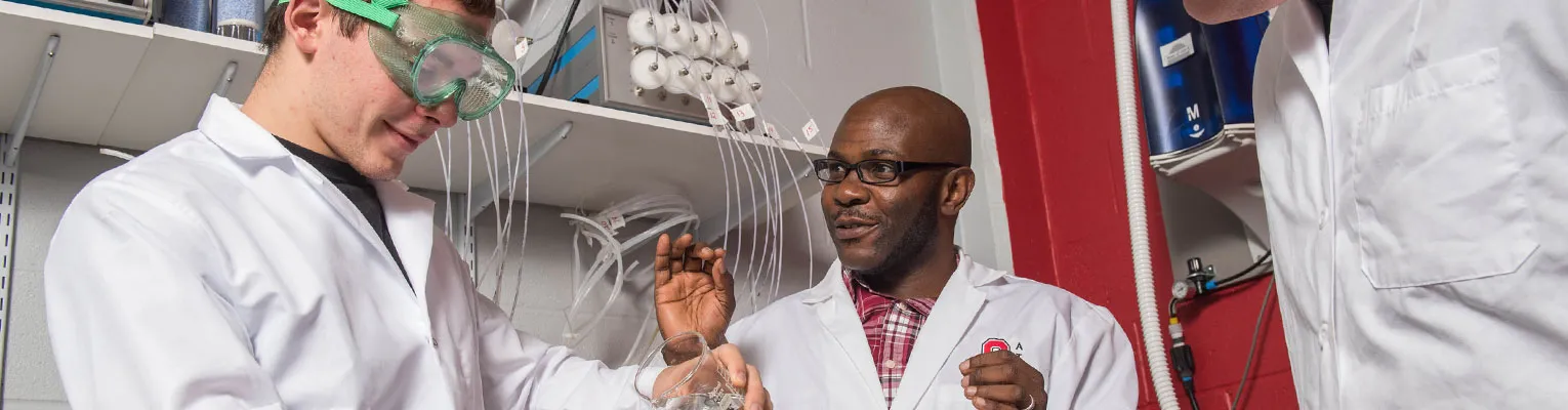 people in lab wearing PPE pouring liquid in a beaker