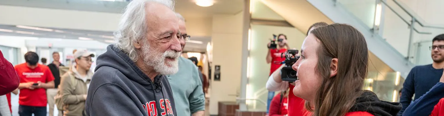 Pierre Agostini speaking to a student while people take video and pictures