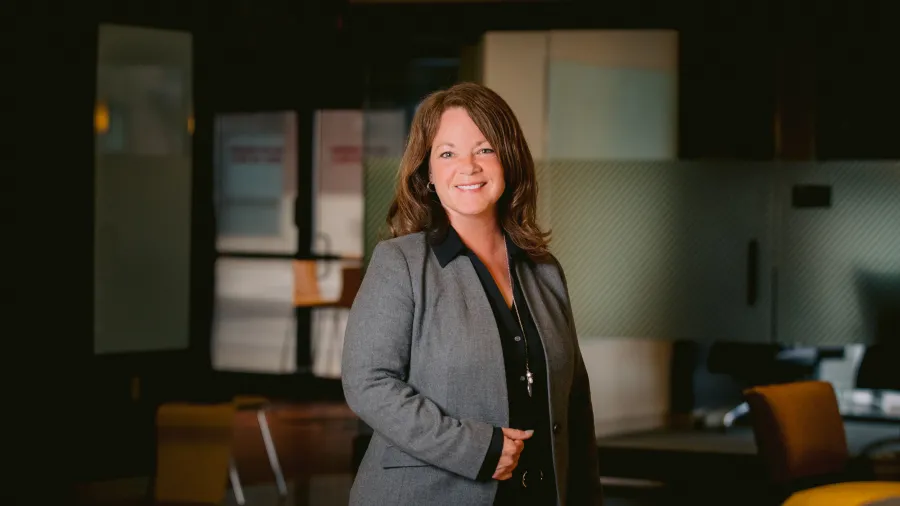Alissa Comella in a dark gray suit standing in an office