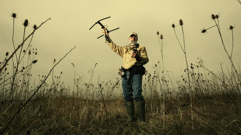 Man standing in field while holding a drone over his head