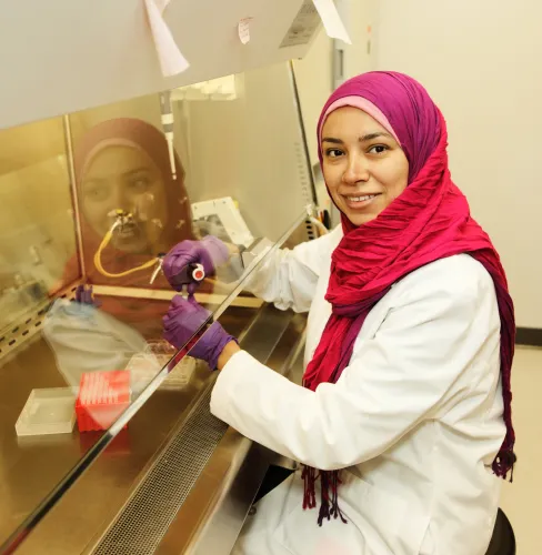 Woman in lab coat working with specimen under a hood
