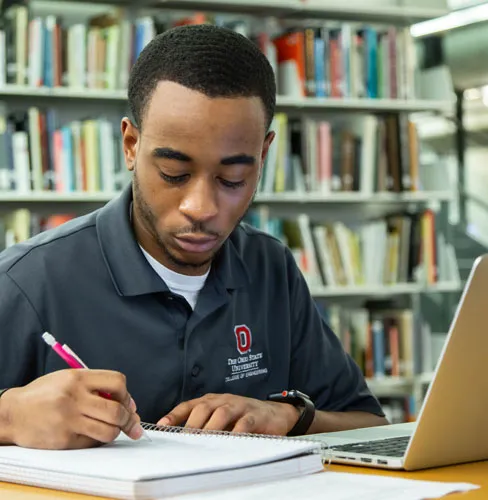 Person note taking with books in the background