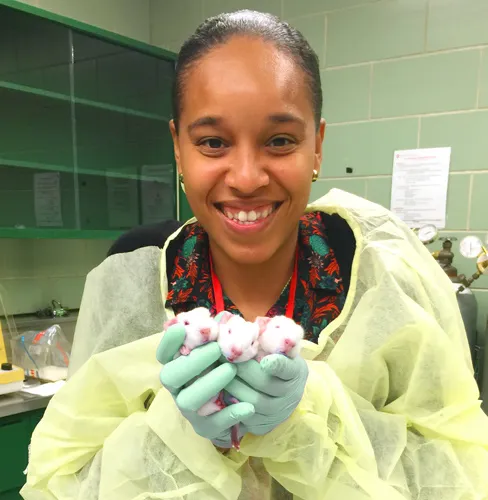 student in scrubs and gloves holding mice in a lab